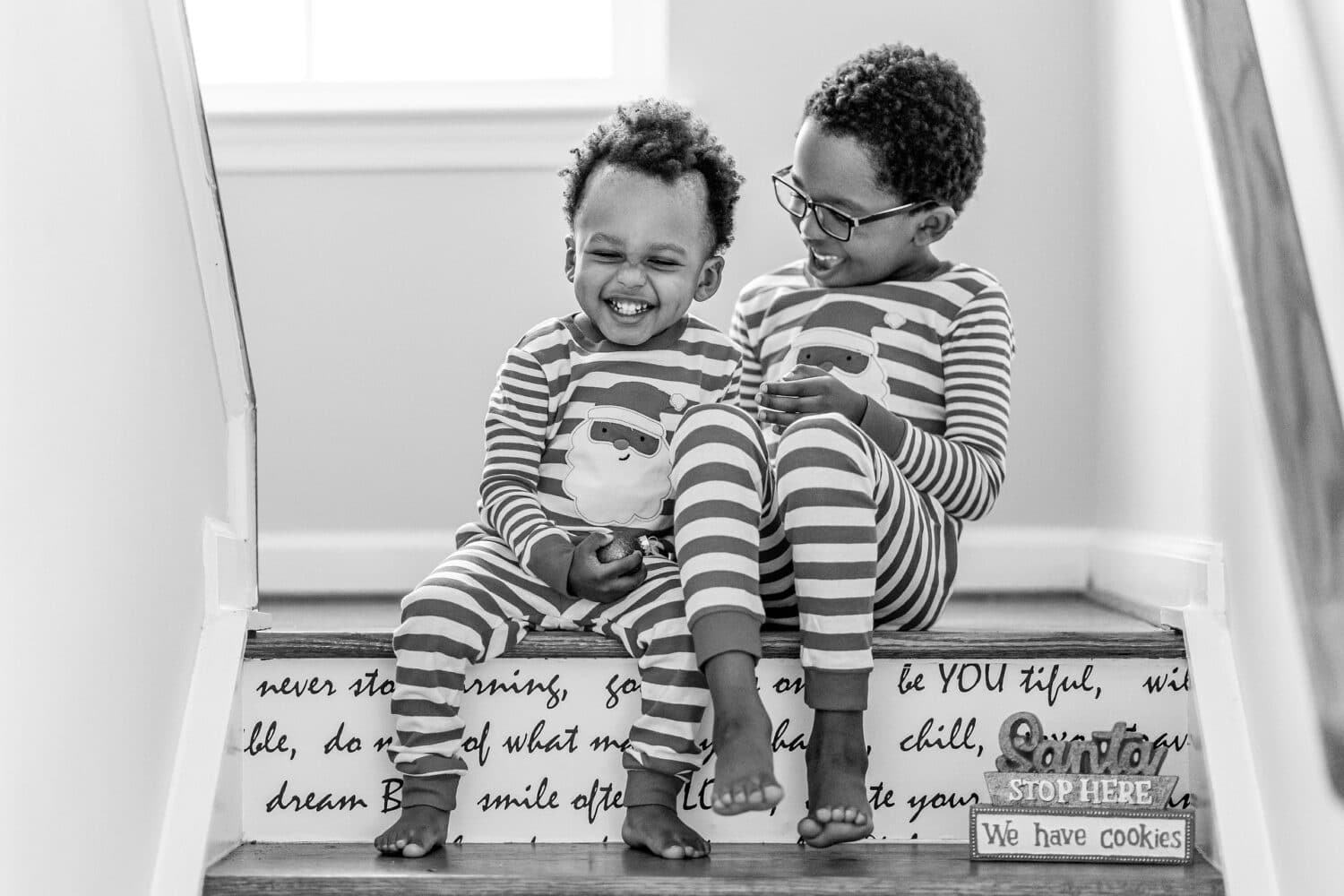 Two boys in matching pajamas sit on stairs laughing