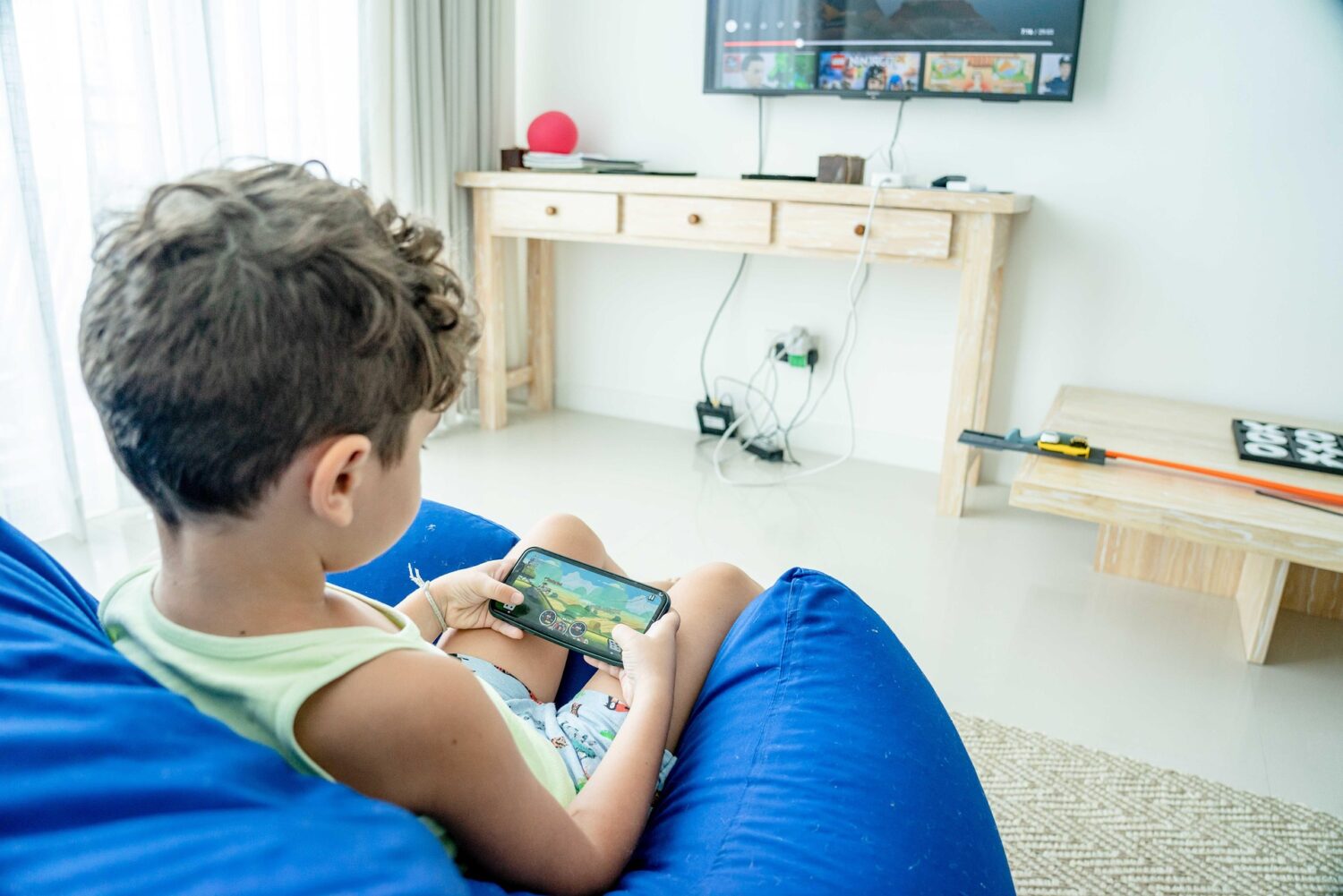 Young boy plays game on mobile phone while sitting in blue chair