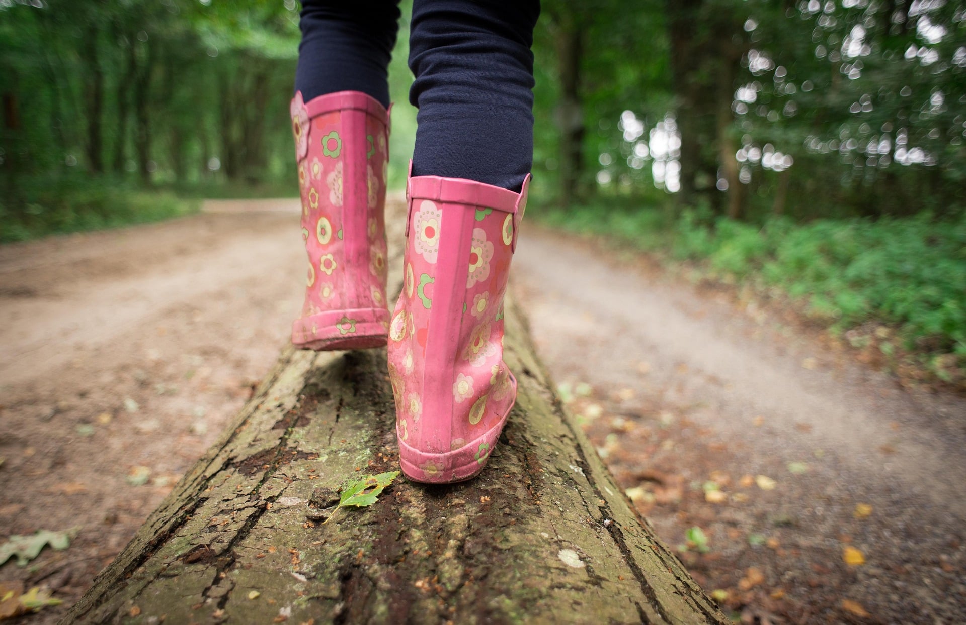 Close up of pink galoshes walking on wooden beam on dirt road