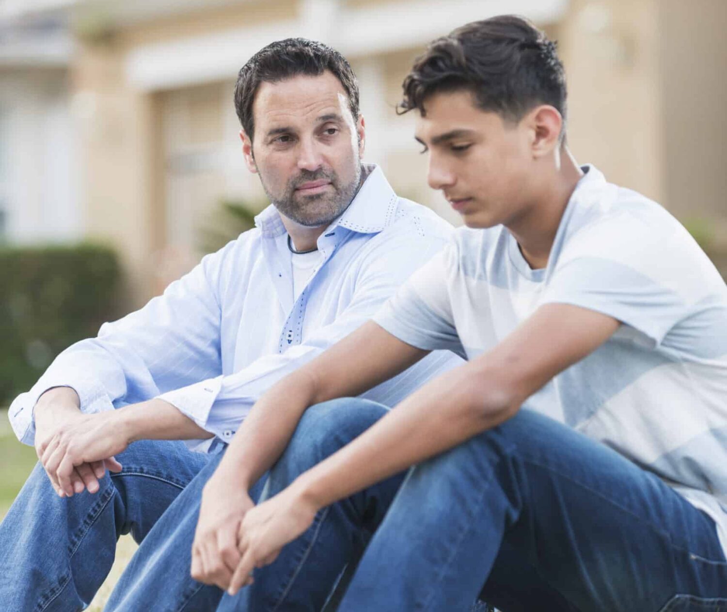 Father and son sitting on ground outside having a conversation