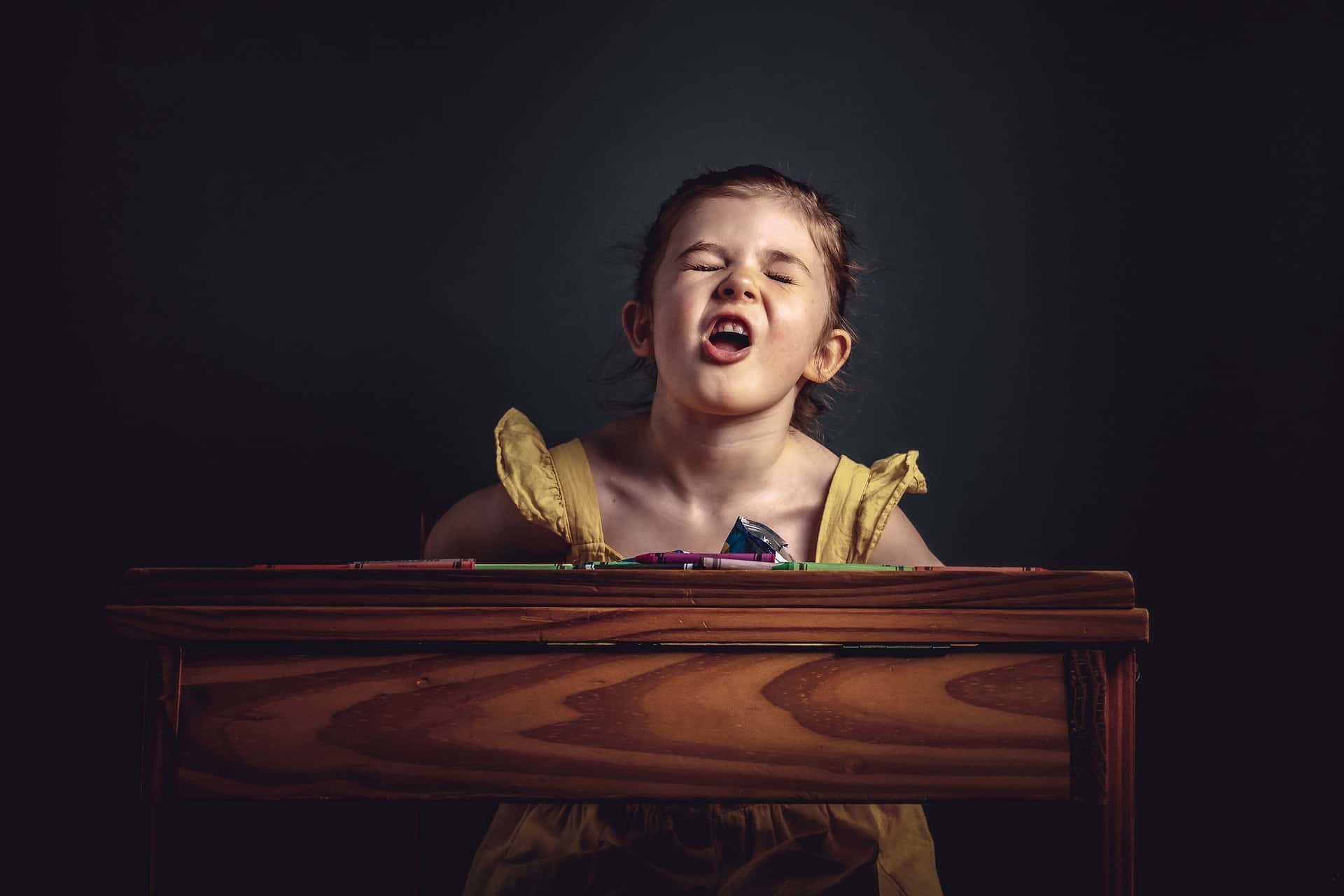 Young girl with frustrated expression sitting at a wooden desk