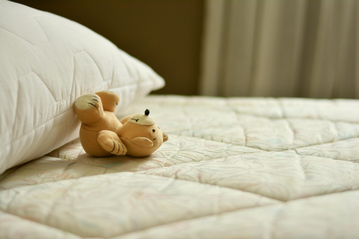 Bare mattress with pillow and stuffed bear