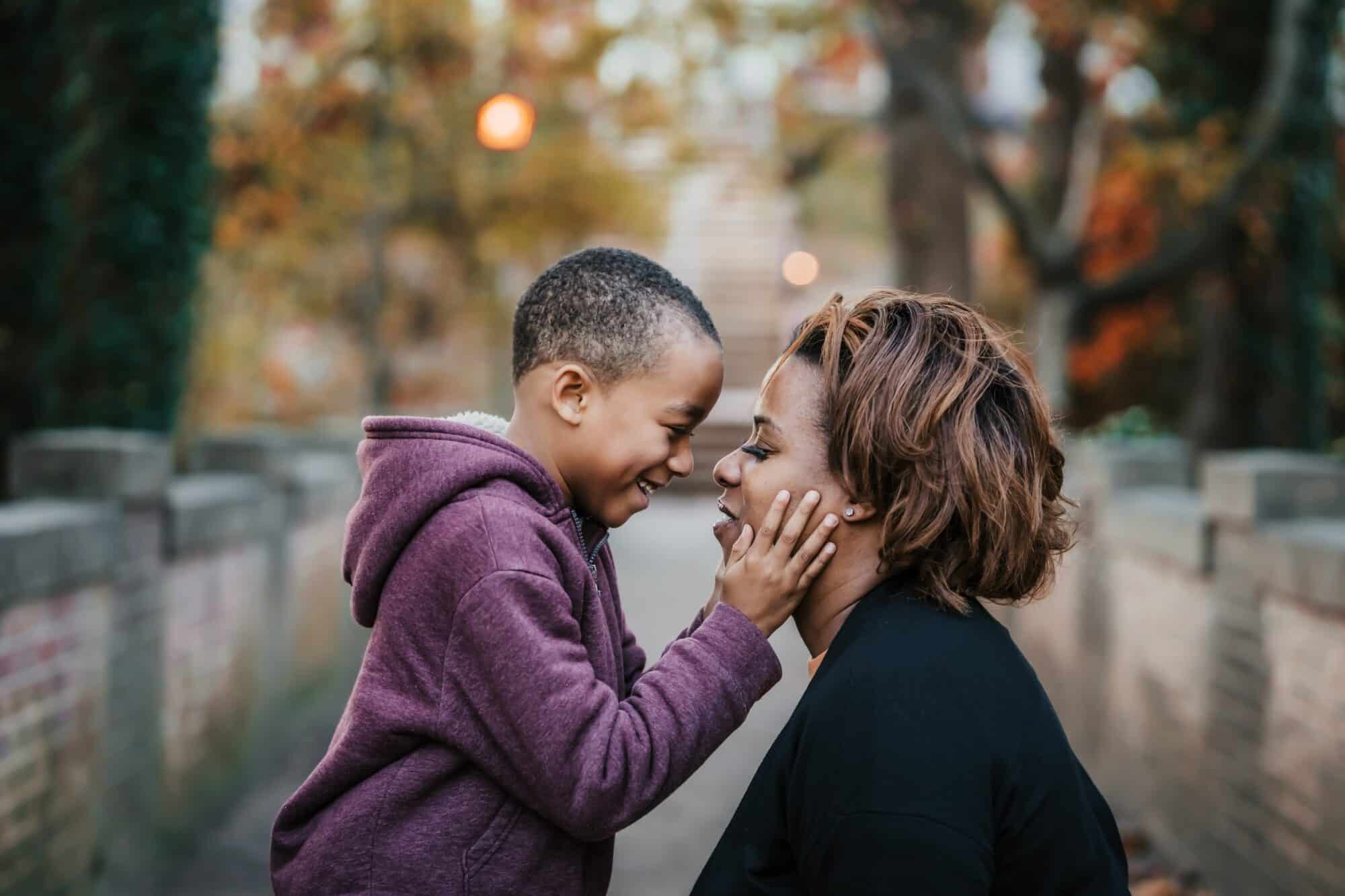 Young boy and female caregiver face to face, laughing in park