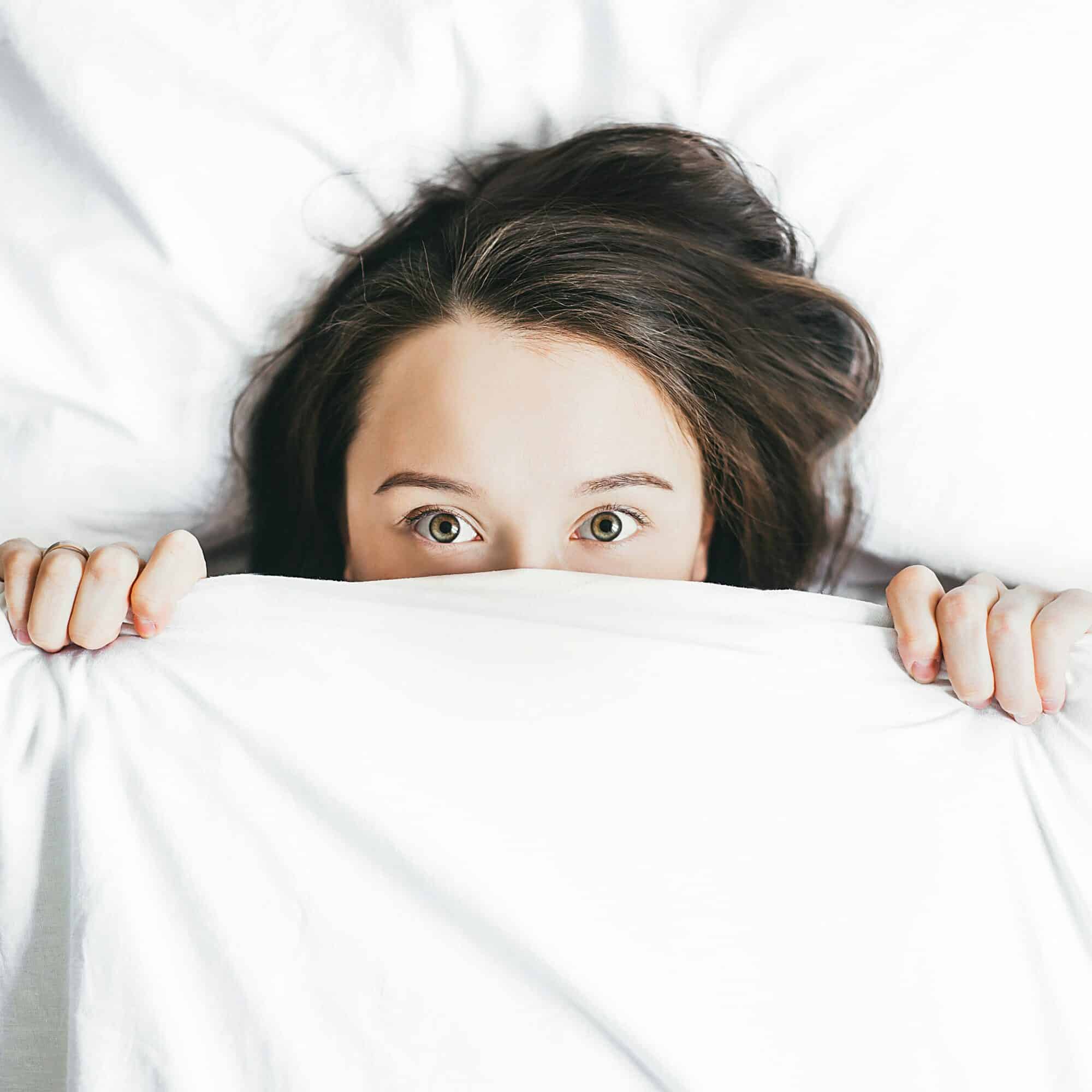 Woman's face and hands peeking out of bed sheet